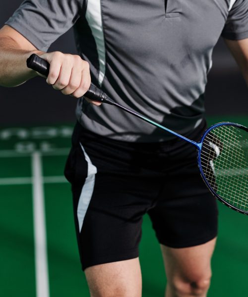 Cropped image of fit young man serving shuttlecock when playing game with friend