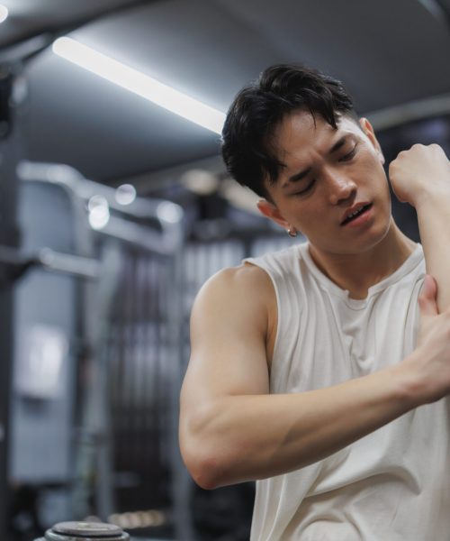 Asian sportsman experiencing elbow pain after an intense workout session at the gym, highlighting the challenges of fitness training and injury